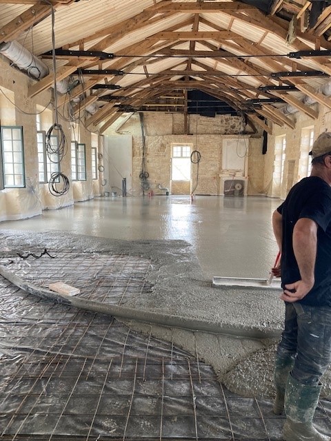 Coulage d'un dallage béton sur treillis soudé dans un bâtiment ancien en pierre avec charpente bois